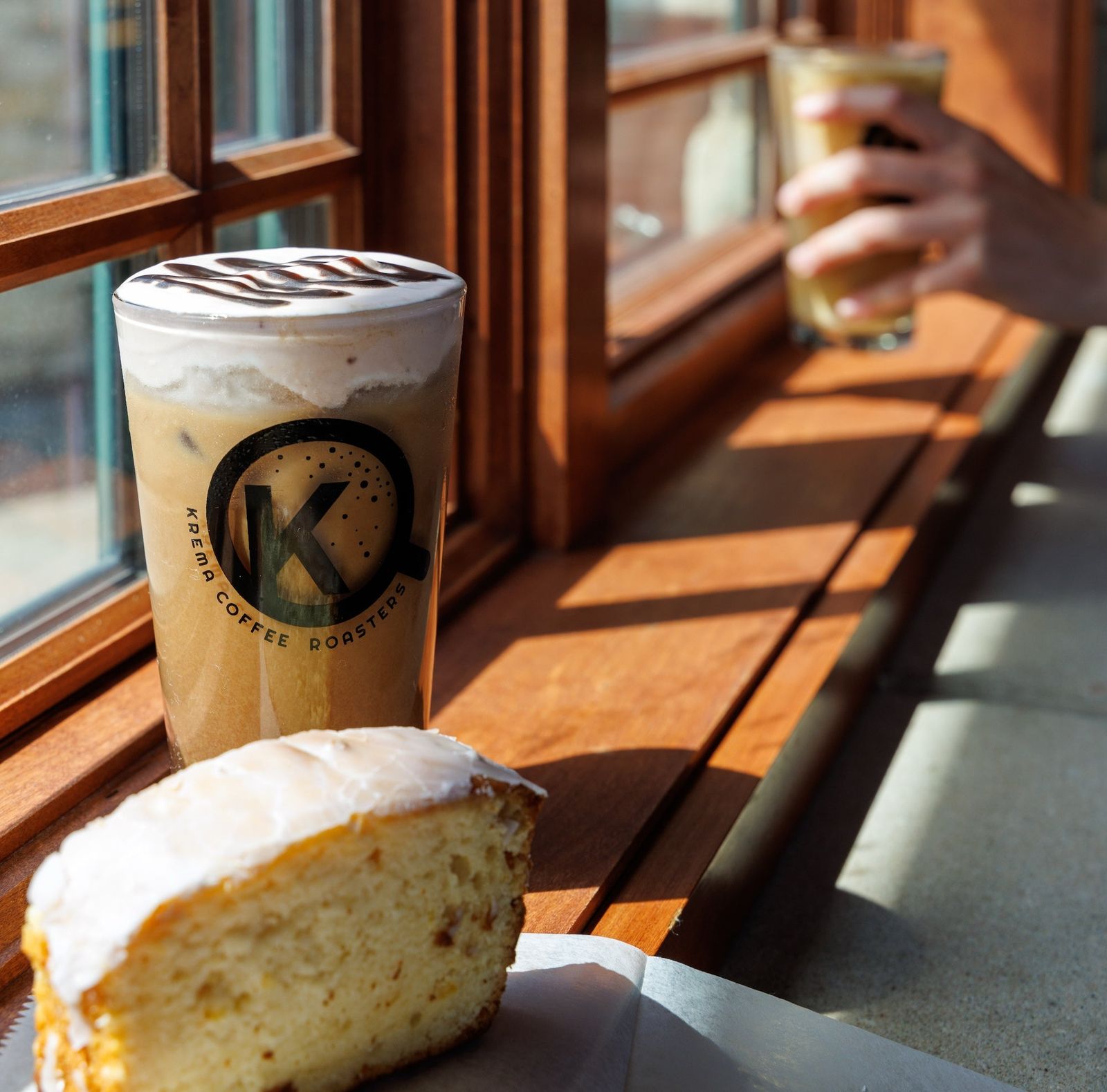 Latte in a Krema cup with a glazed pastry on a sunny window ledge